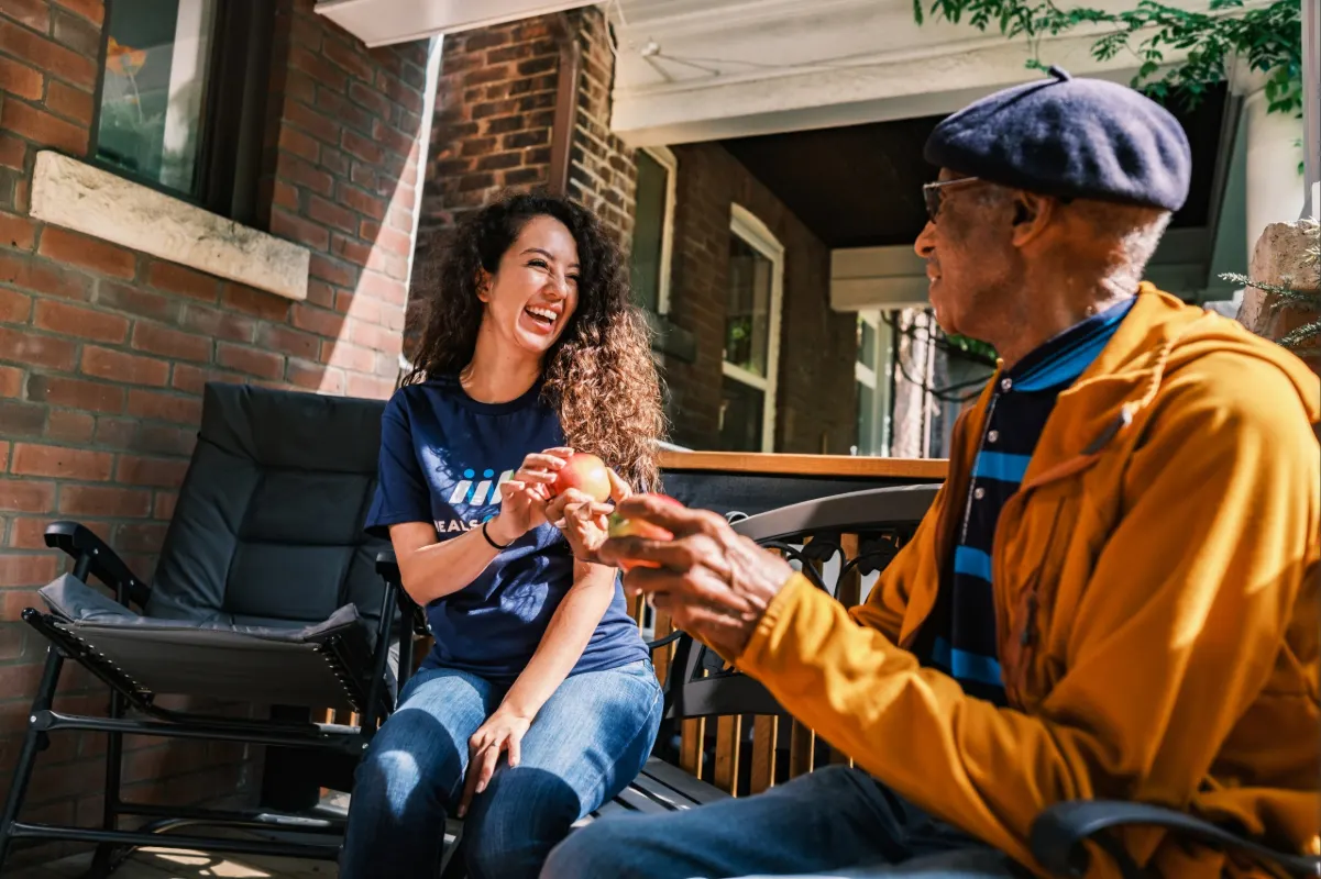 Female volunteer and senior client sharing food on porch.