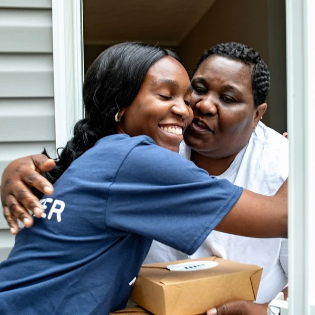 Black Female Volunteer Hugging Happily Black Female Client with Meal Delivery at Door
