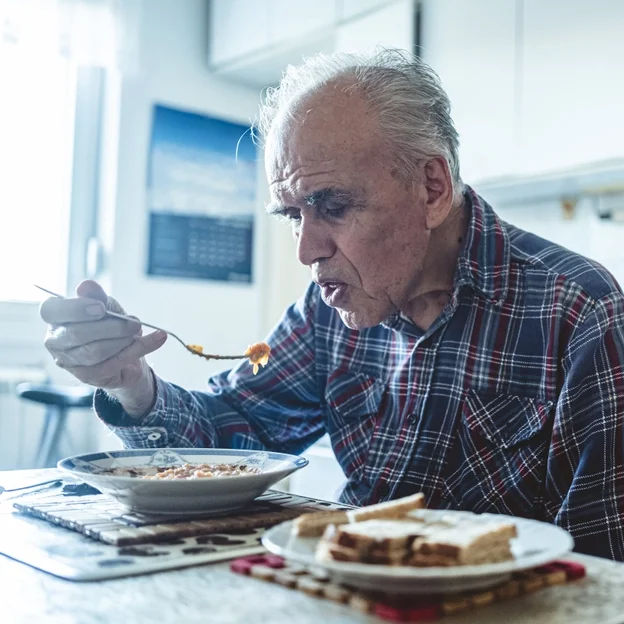 Male Client Plaid Shirt Eating Oatmeal in Kitchen Neutral - Meals on Wheels work in nutrition