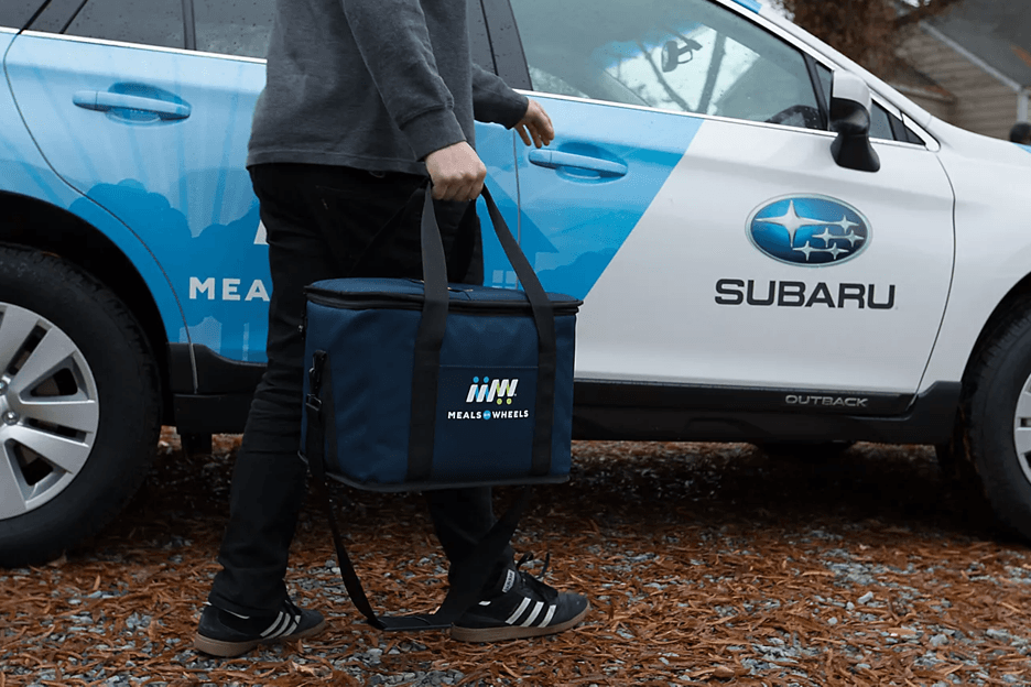 White Male Volunteer Delivering Branded Meal in Front of Subaru Branded Car