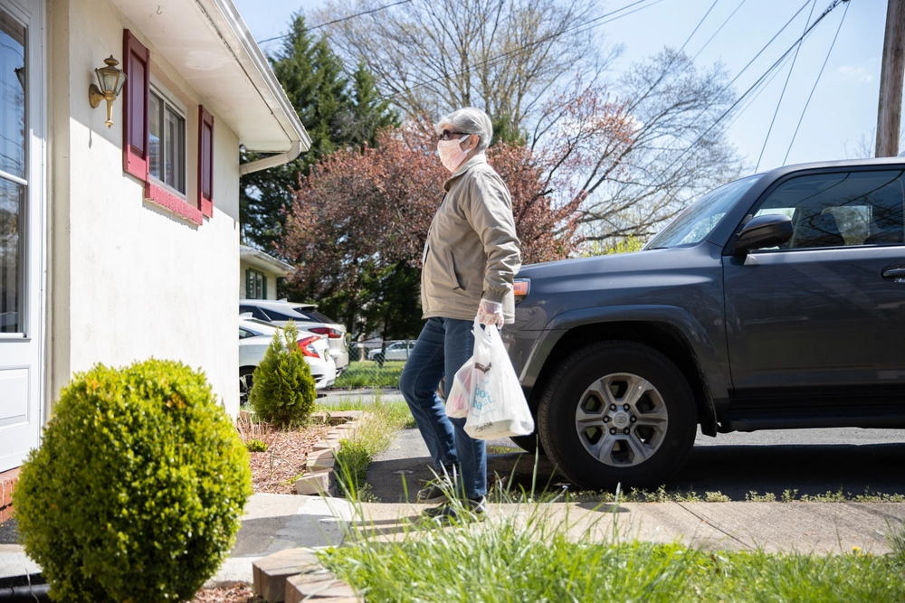 White Senior Female Volunteer in Gray Jacket Delivering Meal in Mask
