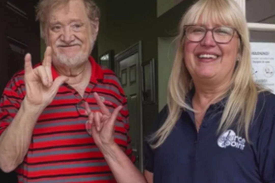Volunteer, Debbie, and deaf client, Dennis showing I Love You in Sign Language