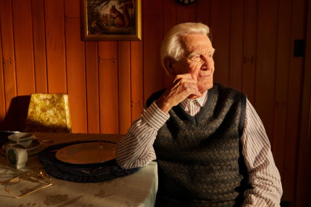 Man at table with empty plate looking out window - senior hunger crisis