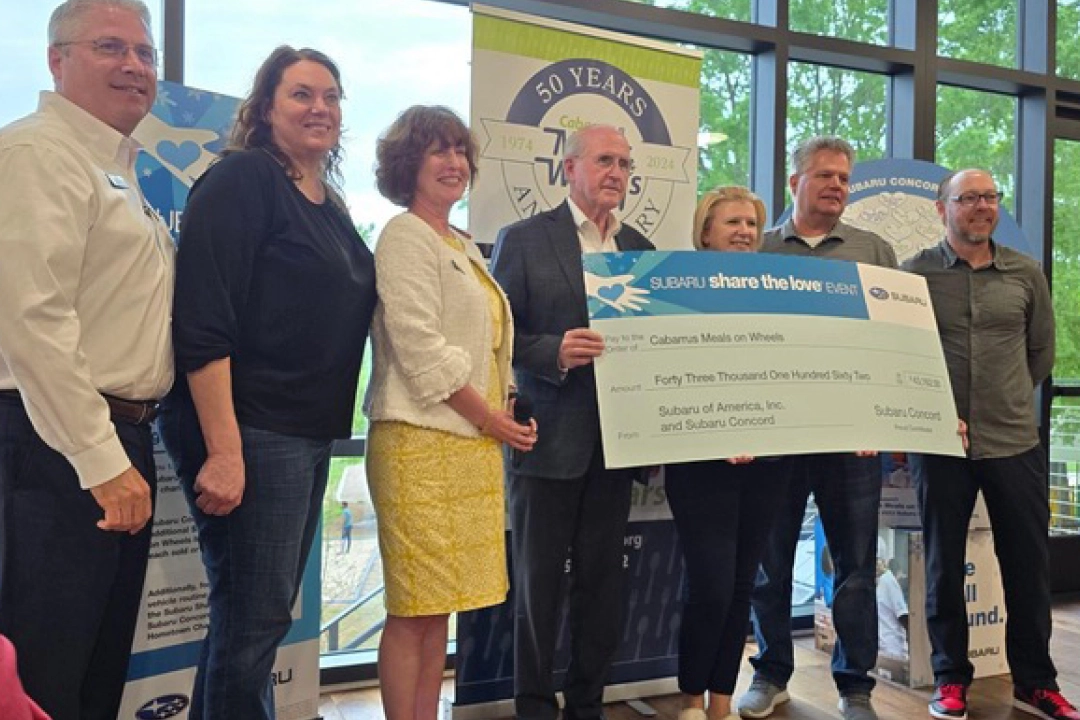 People gathered with Whitney Marti holding a Subaru Share the Love Check - supporting senior wellbeing