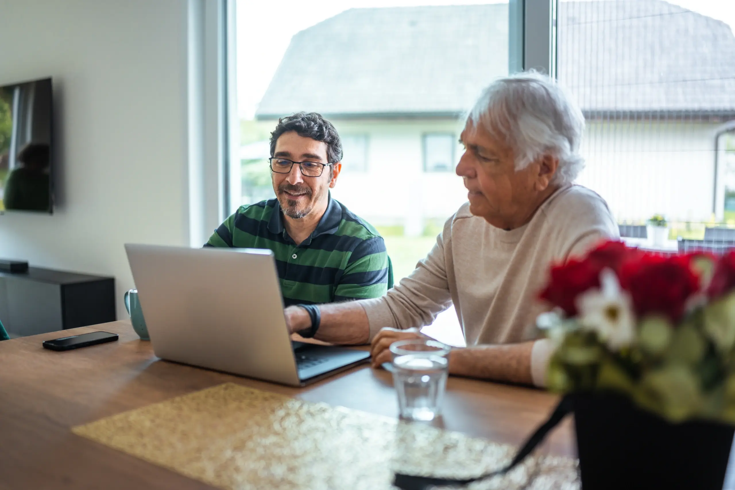 Male with glasses sitting with his father while looking at a laptop.