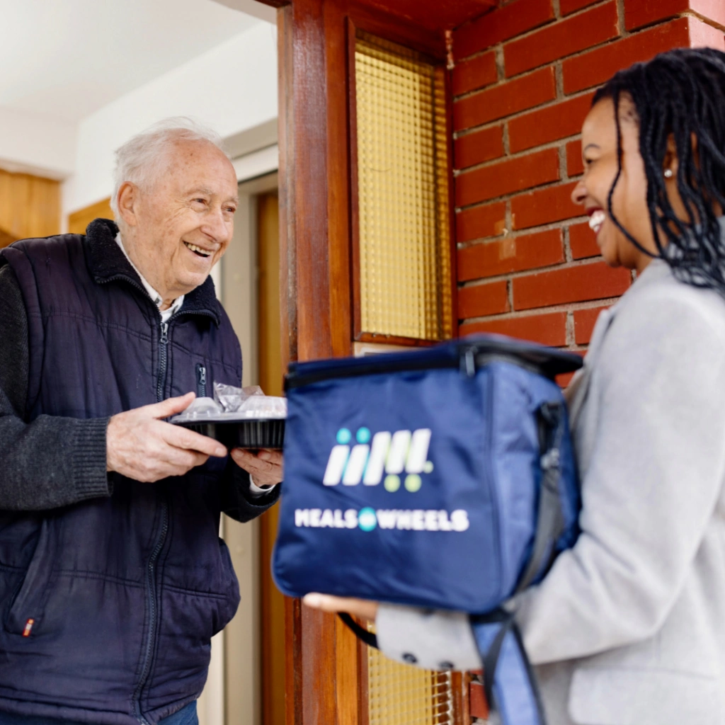 Meals on Wheels volunteer greeting a senior that is holding a meal for Silent Night End the Wait campaign.