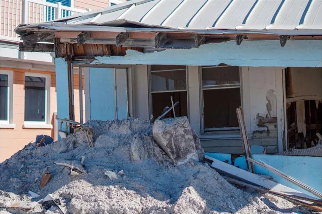 Destroyed house with rubble and torn roof.