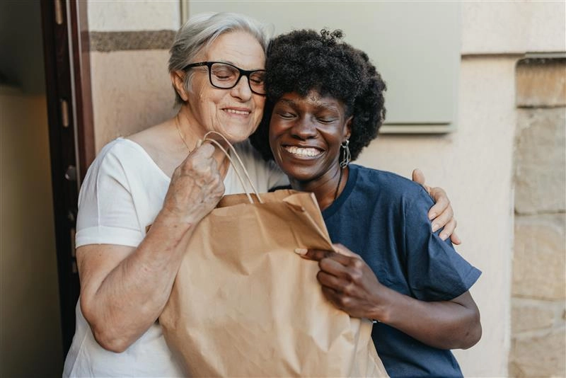 Black volunteer and white senior hugging while holding a senior meal.