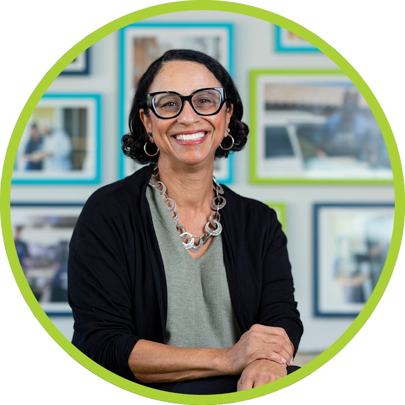 Lynn Gresham smiling wearing sage green top, black blazer, earrings, and a necklace.