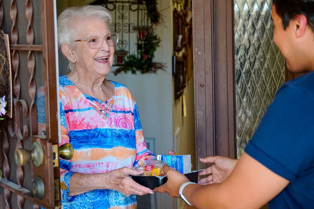 Mrs. Janie, Meals on Wheels Client, receiving meal from volunteer at door.