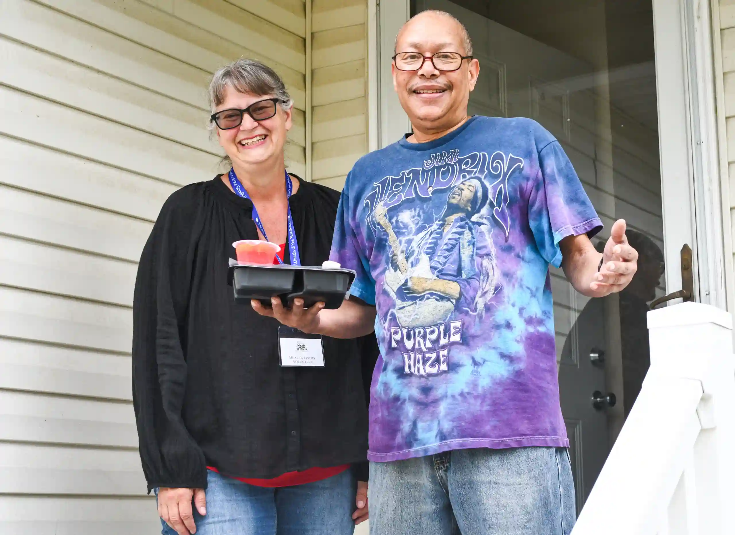 Rodney wearing a blue and purple tie-dye Jimi Hendrix Purple Haze shirt with a female volunteer wearing a black top.