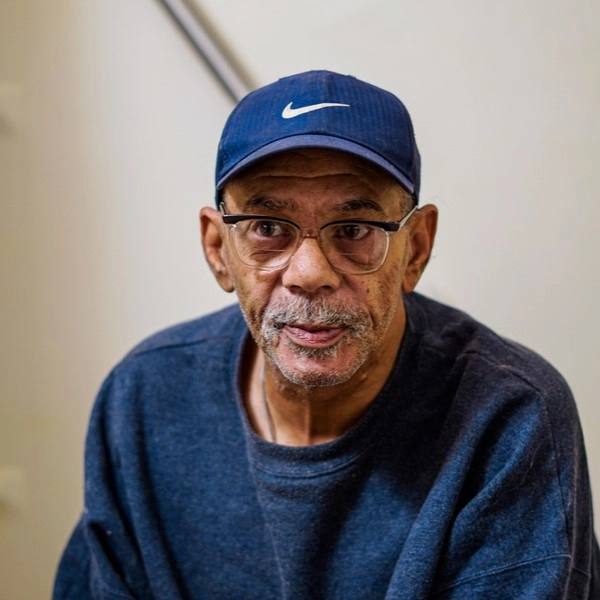 Black male senior wearing glasses, navy-blue sweatshirt, and navy-blue Nike hat.