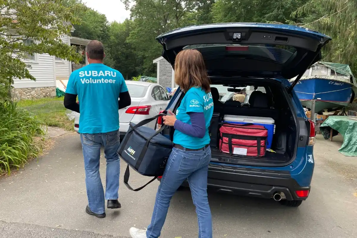 Two Subaru volunteers walking towards a house carrying a meal.