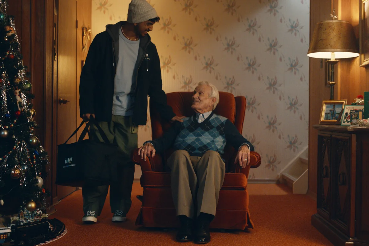 Volunteer with White male senior sitting on an armchair with a Christmas tree next to them.