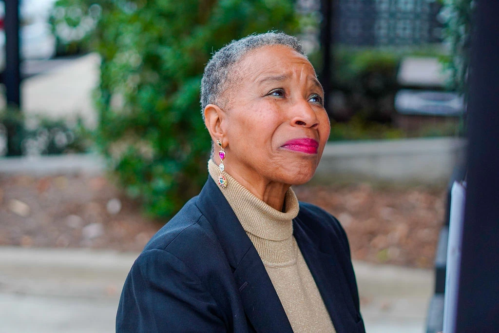 Sonya Mitchell wearing a blazer and light brown turtleneck looking up towards the sky with a smile on her face