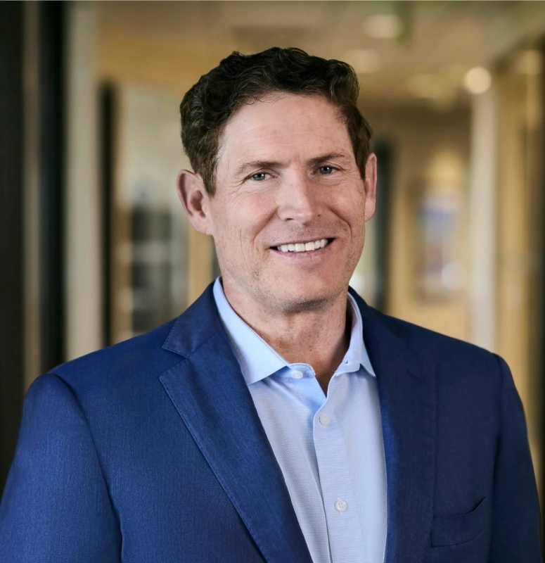 Steve Young smiling while wearing navy-blue suit jacket and light blue button down top.