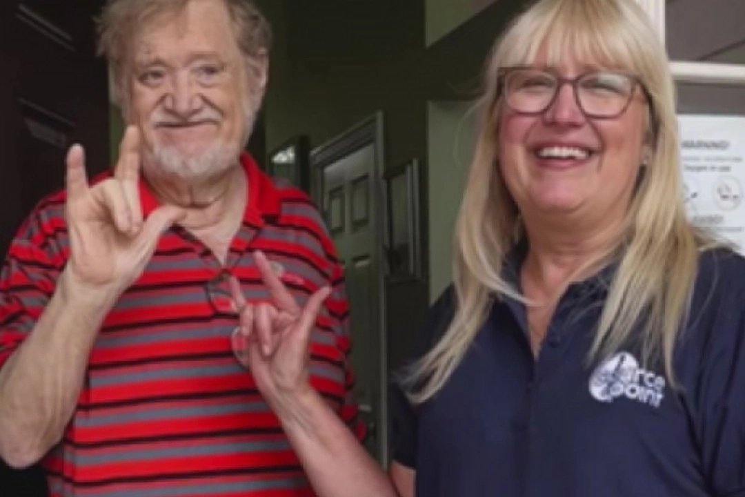 Volunteer, Debbie, and deaf client, Dennis showing I Love You in Sign Language