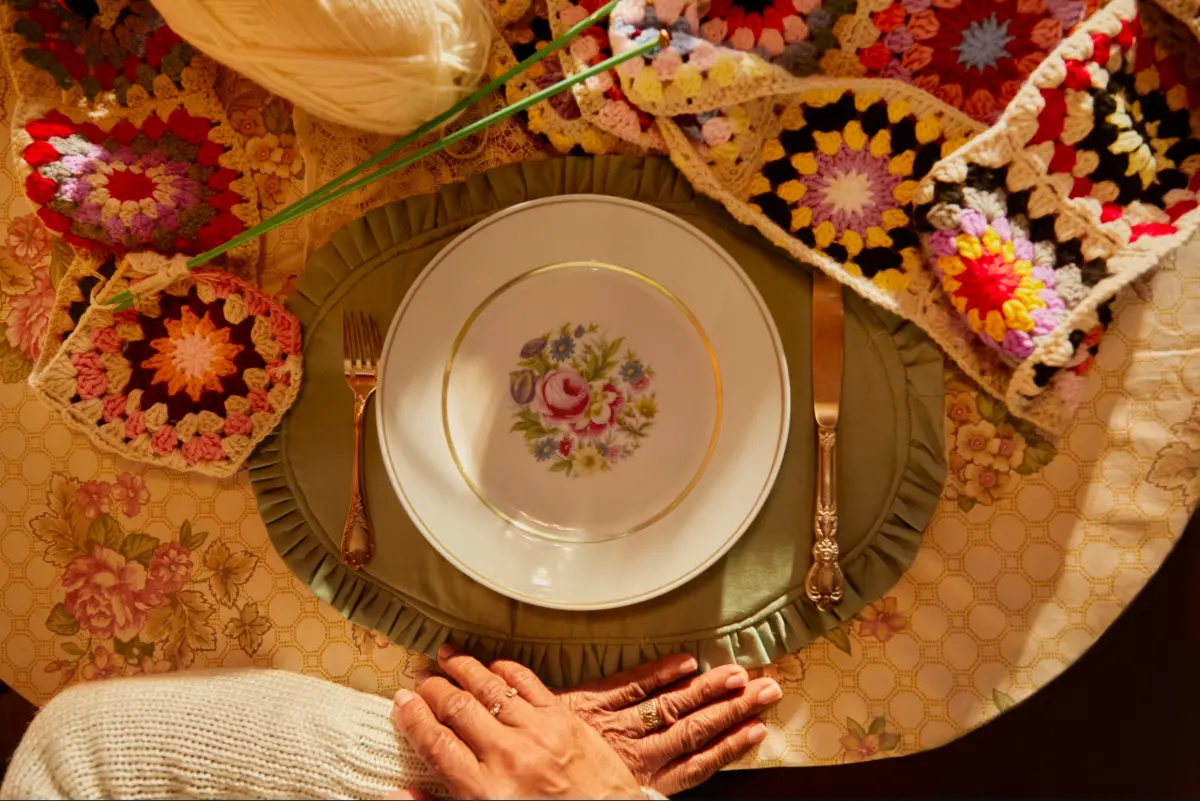 Woman waiting in front of an empty dinner plate with a very long knitted scarf.