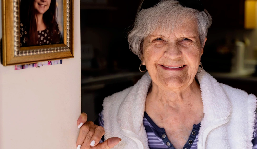 Evelyn, Meals on Wheels client, smiling while wearing striped shirt and white vest.