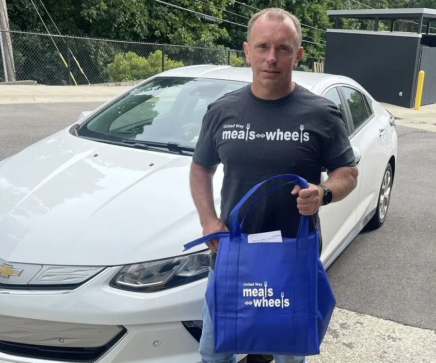 Cassidy Bonner standing in front of car with Meals on Wheels blue bag.
