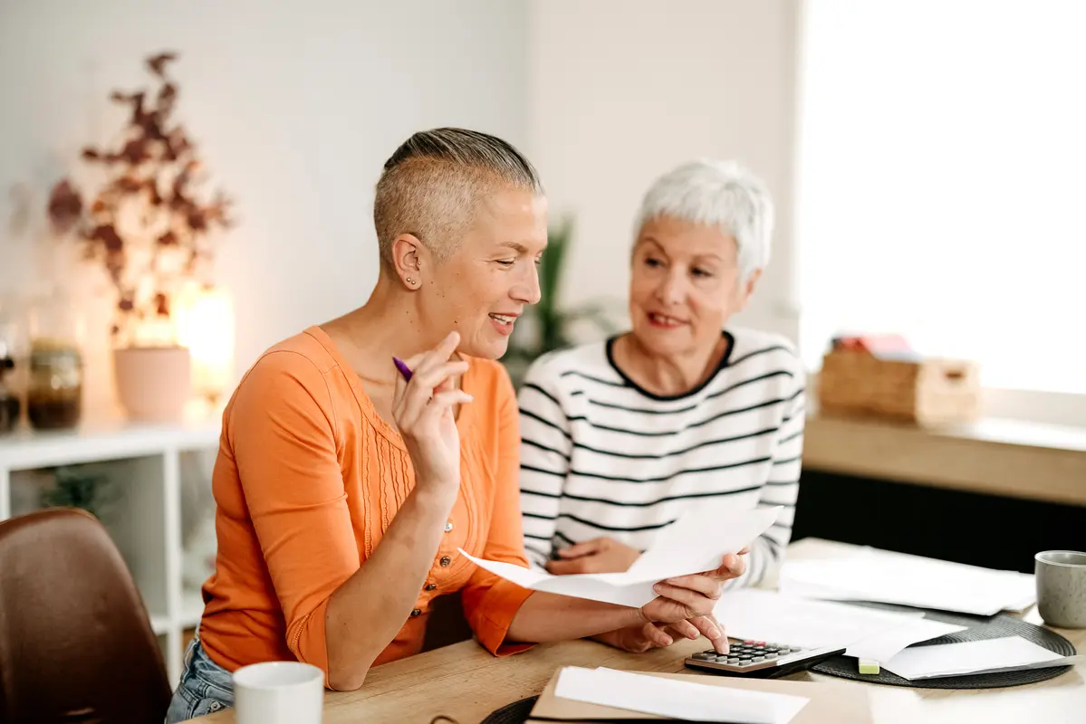 Woman sitting at a table holding a paper smiling while talking to an older adult woman.