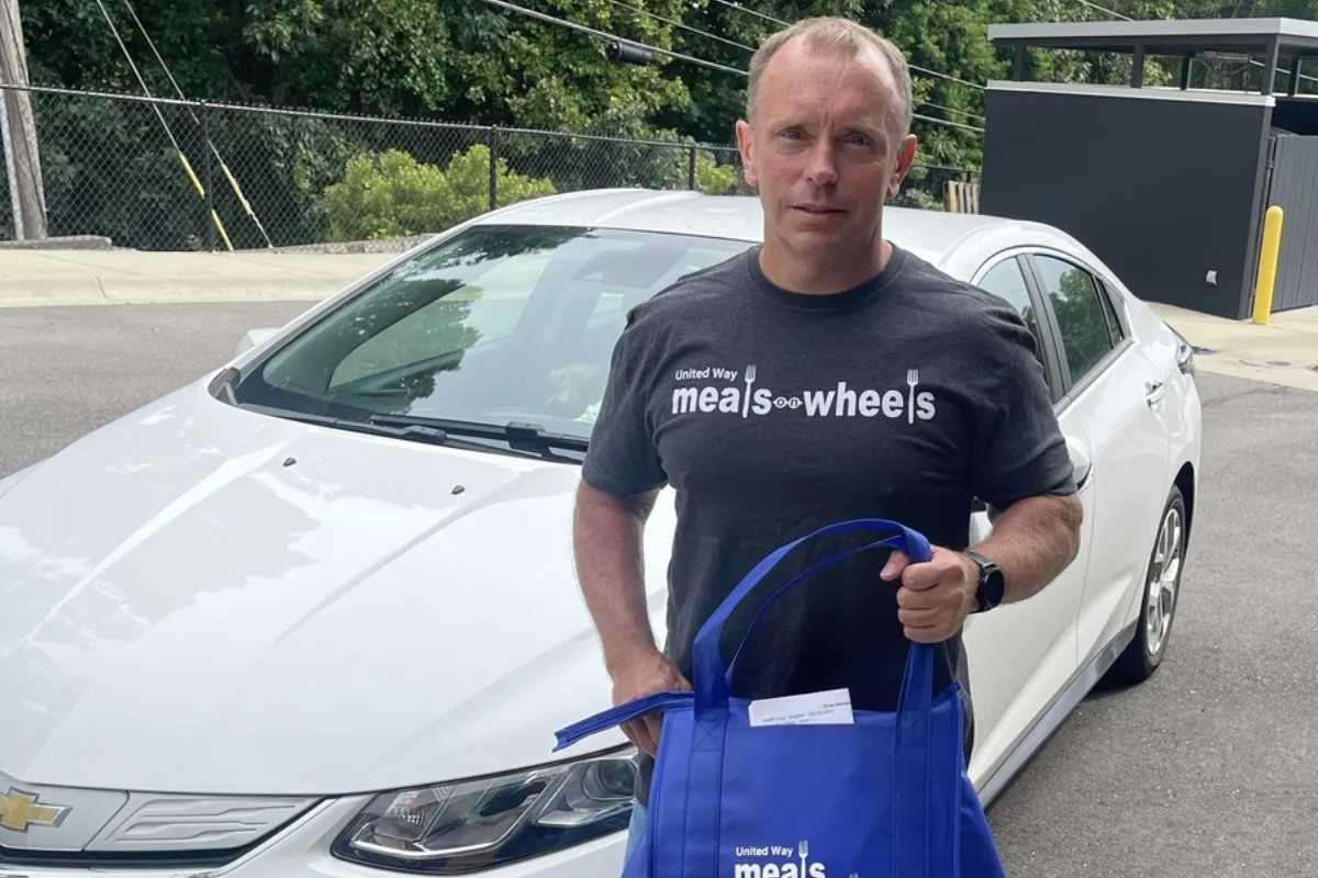 Cassidy Bonner standing in front of car holding a Meals on Wheels blue bag.